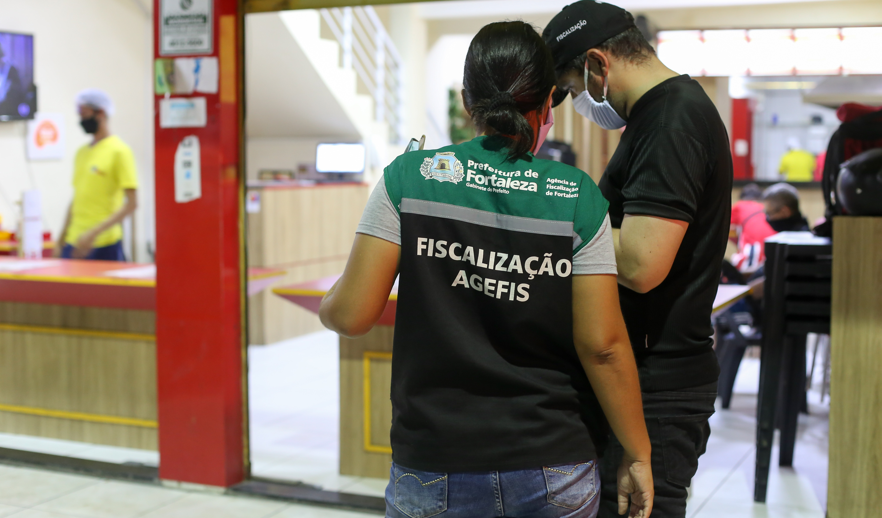 dois fiscais da agefis na frente de um estabelecimento comercial